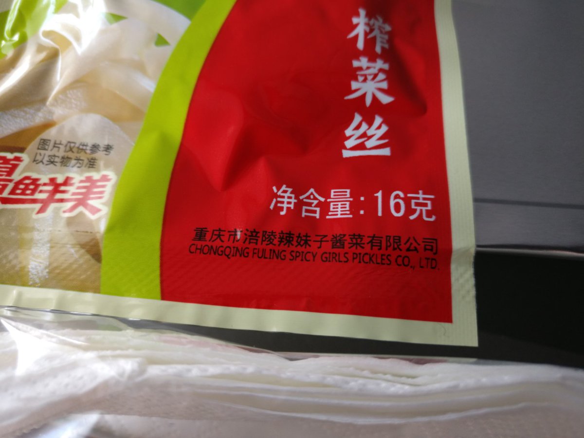 close up of a sealed bag part of an airline meal from mainland china whose manufacturer name is translated as "chongqing fuling spicy girls pickles company limited"