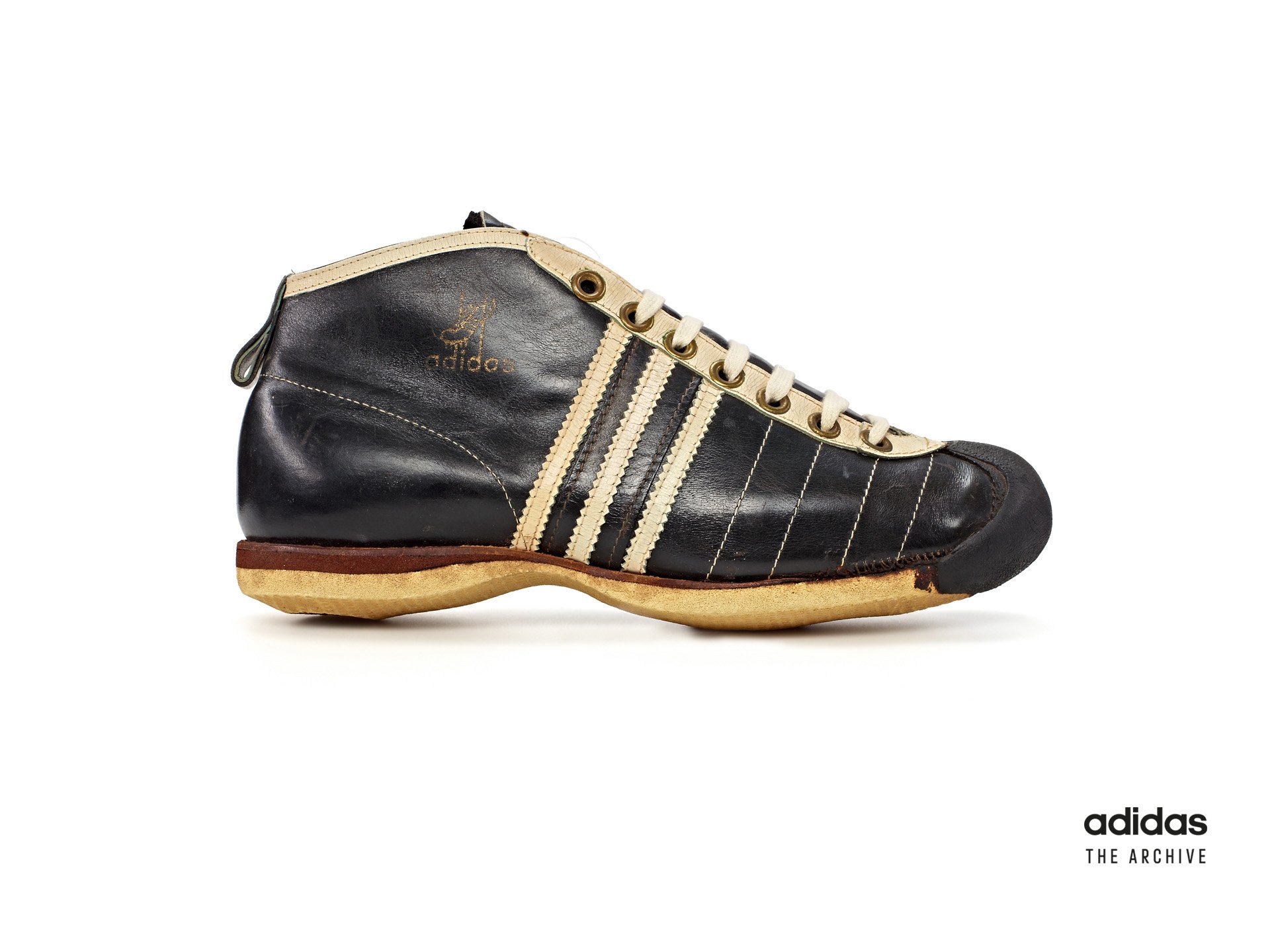 A bulky, black, vintage Adidas soccer shoe with yellowing laces and sole.