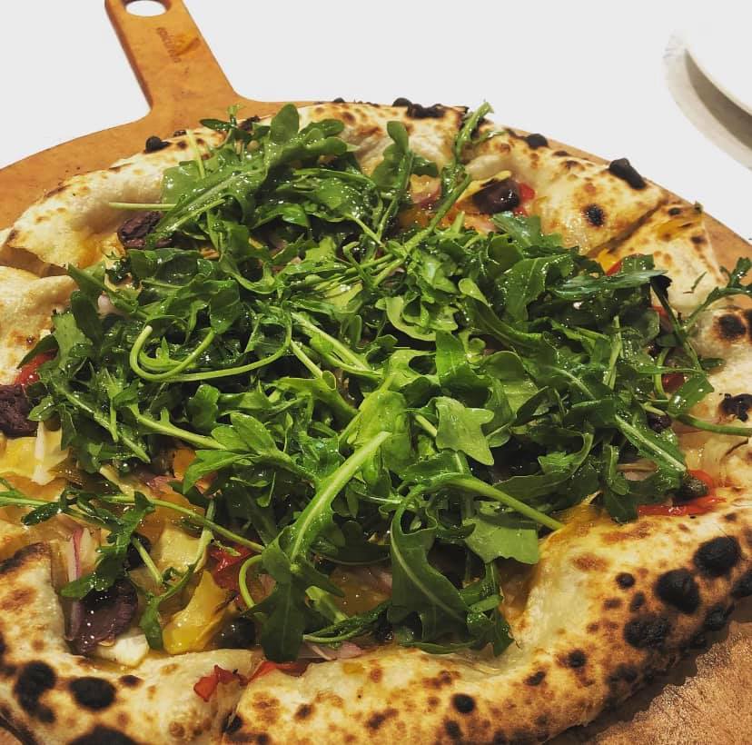 Vegans rejoice - Rad has you covered. We have vegan pizza on our menu - including this artichoke pizza with artichoke hearts, our house-pickled peppers, kalamata olives, onions, and capers topped with a peppery mix of arugula lightly tossed in a vinaigrette.