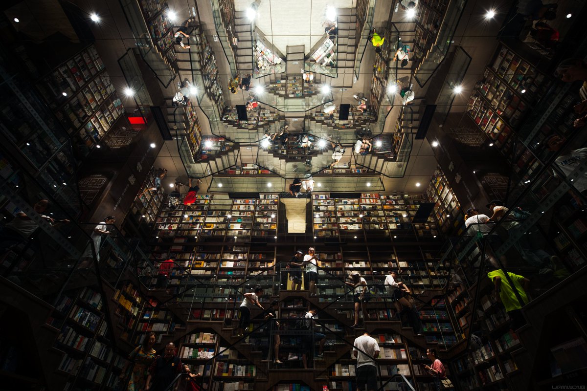 An Inception-like bookstore in Southern China. A large mirror appears on the ceiling, mirroring the interior of the book store, many shelves filled with colorful books.