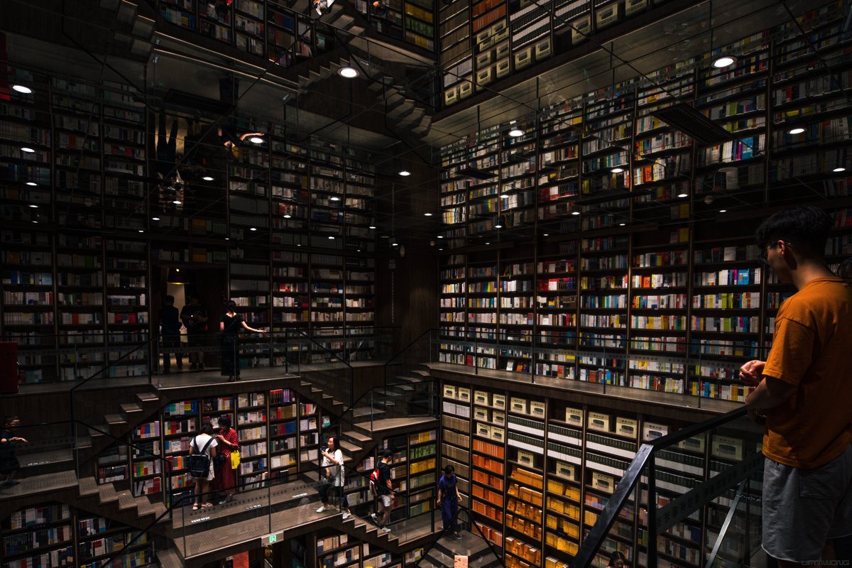 An Inception-like bookstore in Southern China. A large mirror appears on the ceiling, mirroring the interior of the book store, many shelves filled with colorful books.