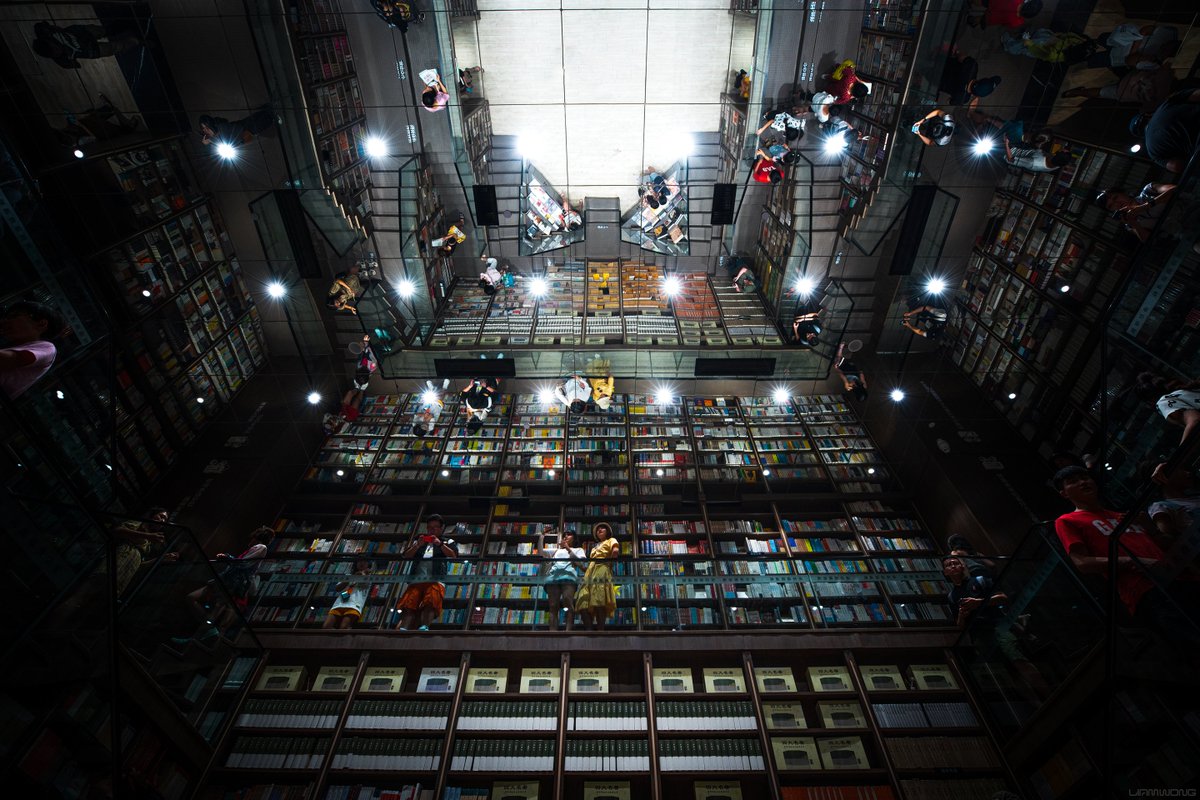 An Inception-like bookstore in Southern China. A large mirror appears on the ceiling, mirroring the interior of the book store, many shelves filled with colorful books.