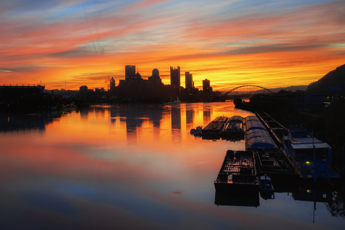 DaveDiCello's tweet photo. The West End Bridge always provides a beautiful view of #Pittsburgh, and when the Ohio River is this smooth, it's an added bonus. Not only is the colorful sunrise reflecting in the water, but also on the barges, giving the entire scene the perfect golden glow. https://t.co/dsE5fYoAdO