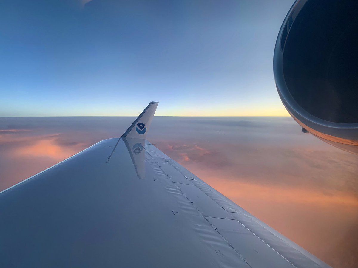 The wing of a NOAA plane is shown high above clouds.