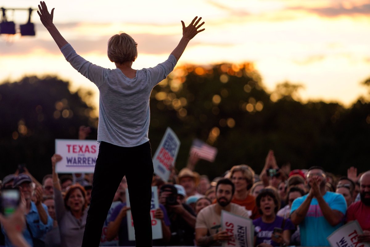 Elizabeth Warren cheers with a crowd of supporters while the sun sets in the background