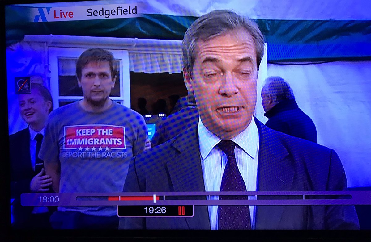 artofthestateuk's tweet photo. Keep The Immigrants, Deport The Racists. Nice little unexpected intervention behind Nigel Farage during a live broadcast on BBC #nigelfarage #BrexitParty :-) https://t.co/FKB7cf5VoS