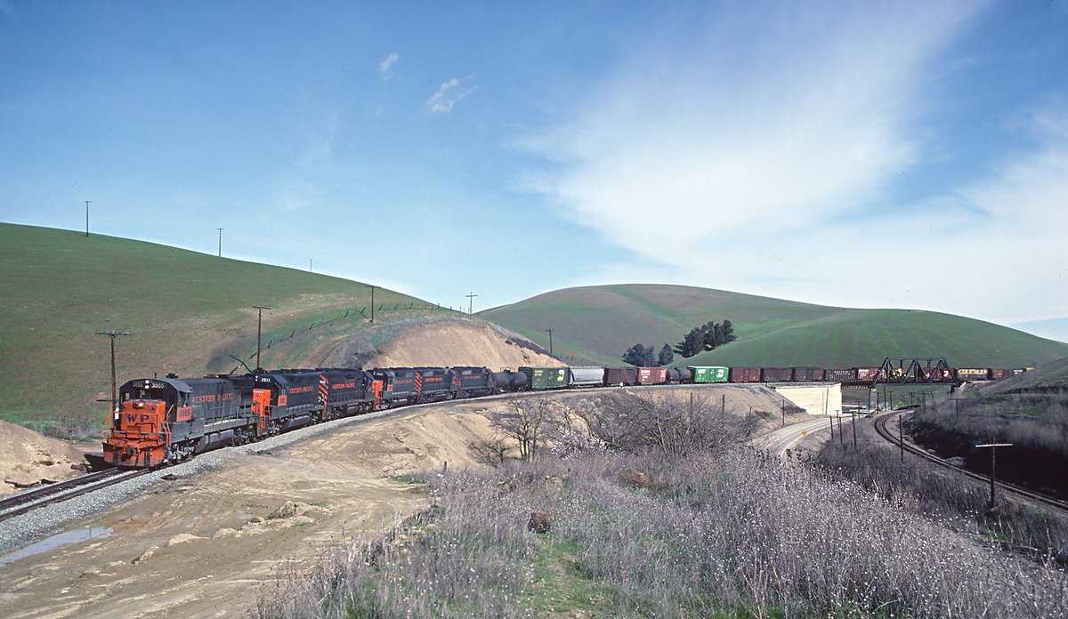 Western Pacific U30B #3055 and several EMD units lead a long freight over the Southern Pacific on Altamont Pass in March, 1981. Roger Puta photo.