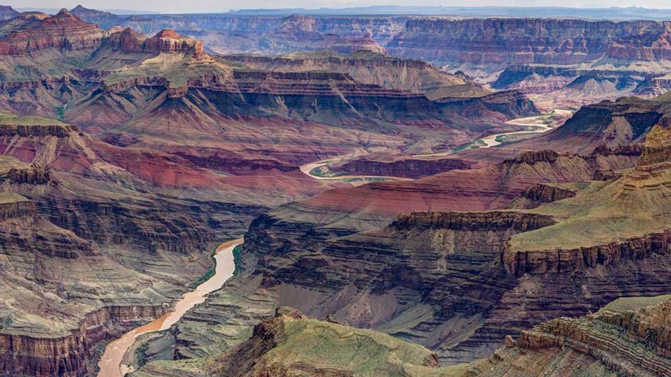 Description: A muddy river meandering through a complex desert landscape of stratified cliffs and ridgelines. NPS/W.Tyson Joye