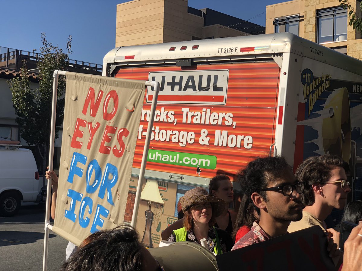 ‪No Eyes for ICE banner & one of four trucks Palantir rented to block the view of the protest‬