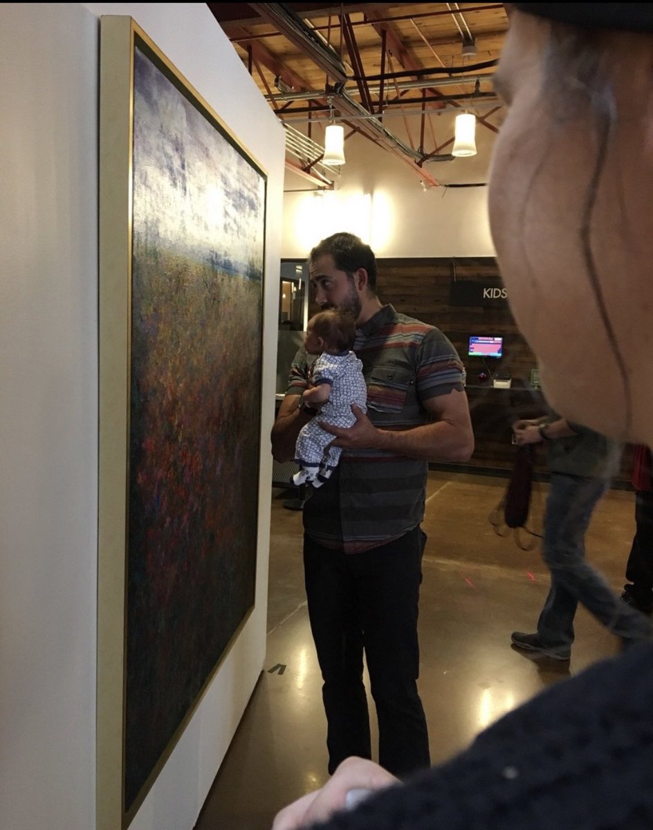 BAAlbaroud's tweet image. A man holding his baby up to paintings and talking to him at an art gallery