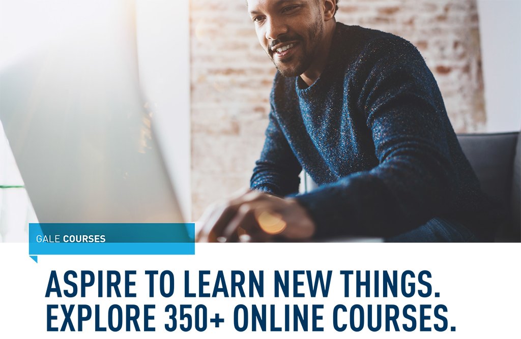 a man smiling sitting on a couch looking down at his laptop in front of him, on a coffee table