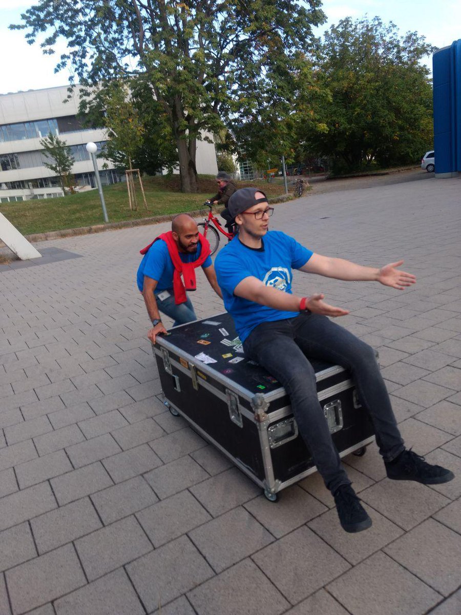 one person sitting on a case, another person pushing it