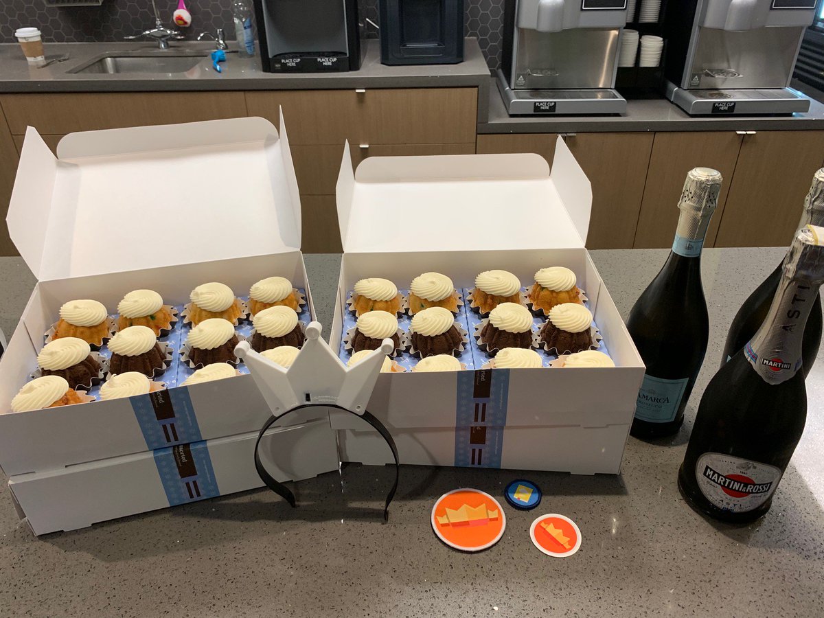 2 boxes of cupcakes next to 3 bottles of champagne.