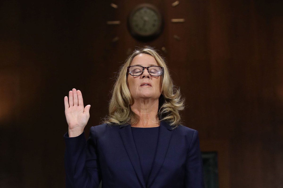 A photo of Dr. Christine Blasey Ford testifying with her hand up and her eyes closed