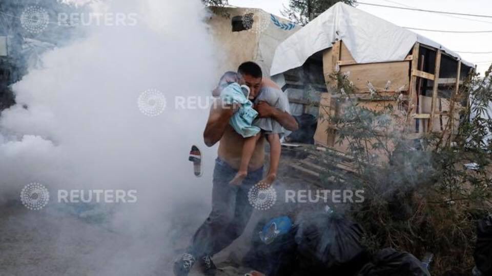 A migrant carries a boy as they flee tear gas fired by riot police during a demonstration, following a fire in Moria camp on the island of Lesbos, Greece, September 29, 2019. REUTERS/Giorgos Moutafis