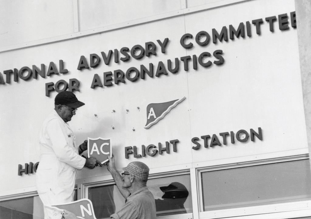 Workers take down the NACA sign to make way for NASA.