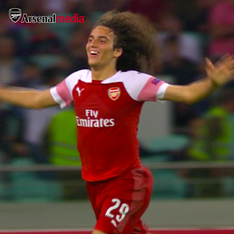 A young Arsenal player with curly hair, wearing the red and white kit with "Fly Emirates" sponsorship and the number 29 on his shorts, celebrates joyfully with arms outstretched, commemorating Arsenal's 3-0 Europa League victory over Qarabag eight years ago.