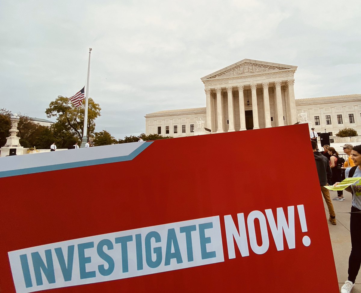 A sign in front of the Supreme Court says “Investigate Now!”