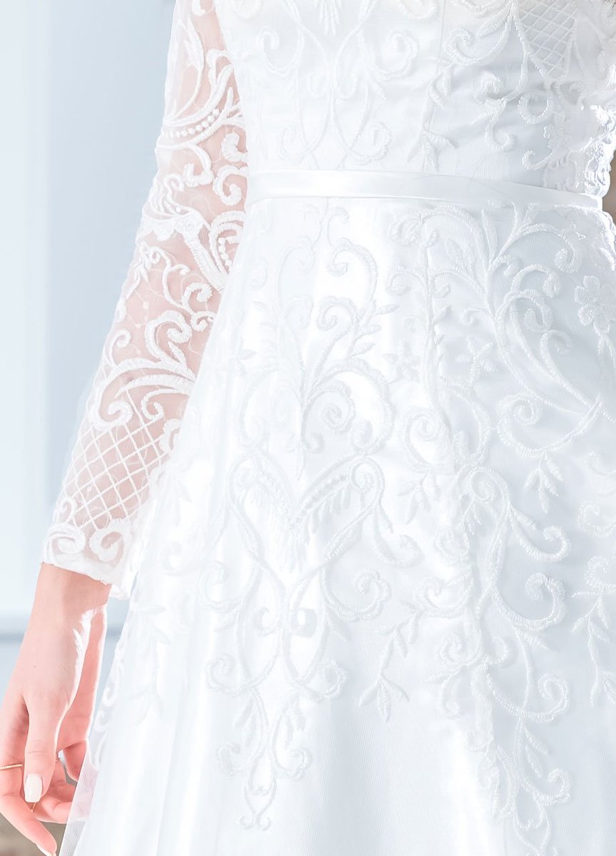 This perfectly classic and traditional lace and tulle full A-line gown offers illusion lace long sleeves over modesty cap sleeves, a curved V-neckline, a satin natural waistband, a back zipper, and a court train.