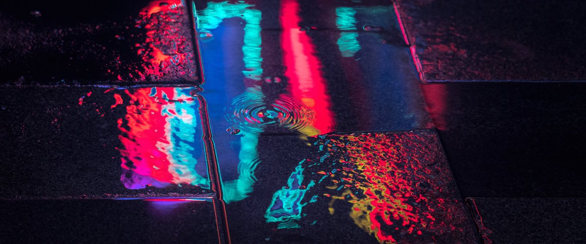 Photography by Liam Wong of Seoul at night. A puddle. It is blue in color and is surrounded by bokeh from the raindrops and lights.