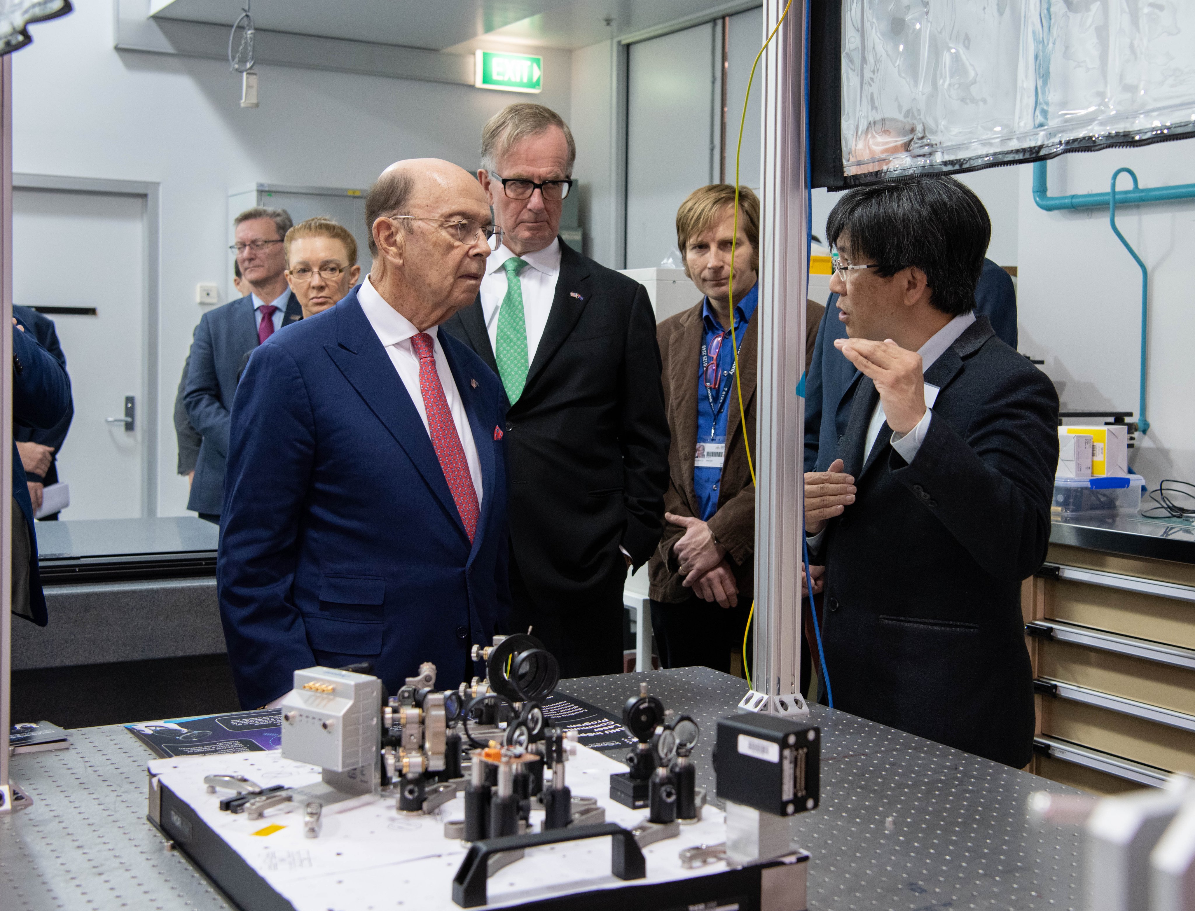 Secretary Ross listening to a person gesturing with equipment in an engineering lab