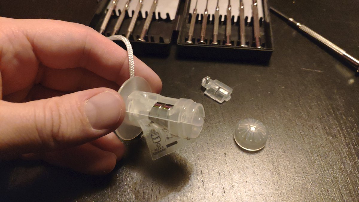 MoonSpir's tweet photo. Those things are basically a two piece shell with a separate battery tray, a sticked on diffuser, two lithium button cells, an LED and a piece of metal that acts as a crude switch. A sticky lable keeps everything together. And a screw for the battery case. #estuff https://t.co/zzQj0A27lB