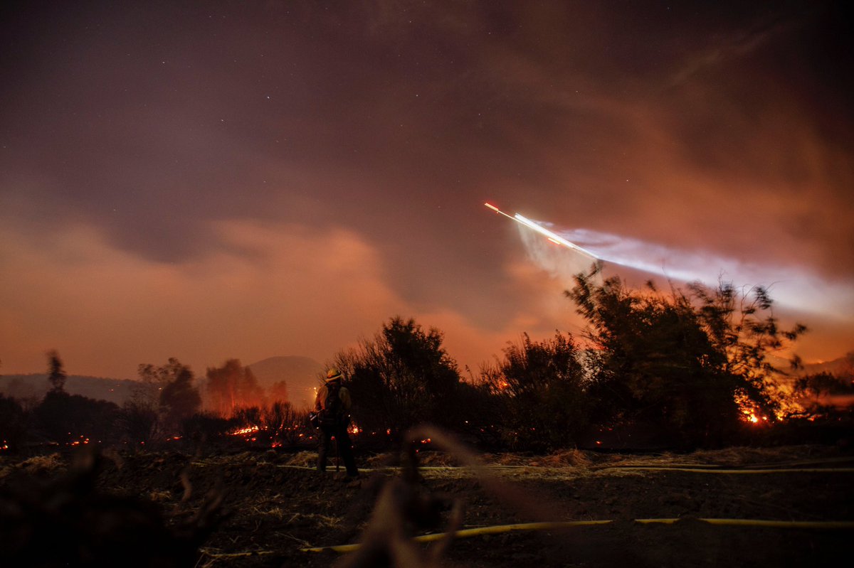 A helicopter flies overhead as firefighters build a hose line to contain the #saddleridgefire 📸 @latimes @latimesphotos