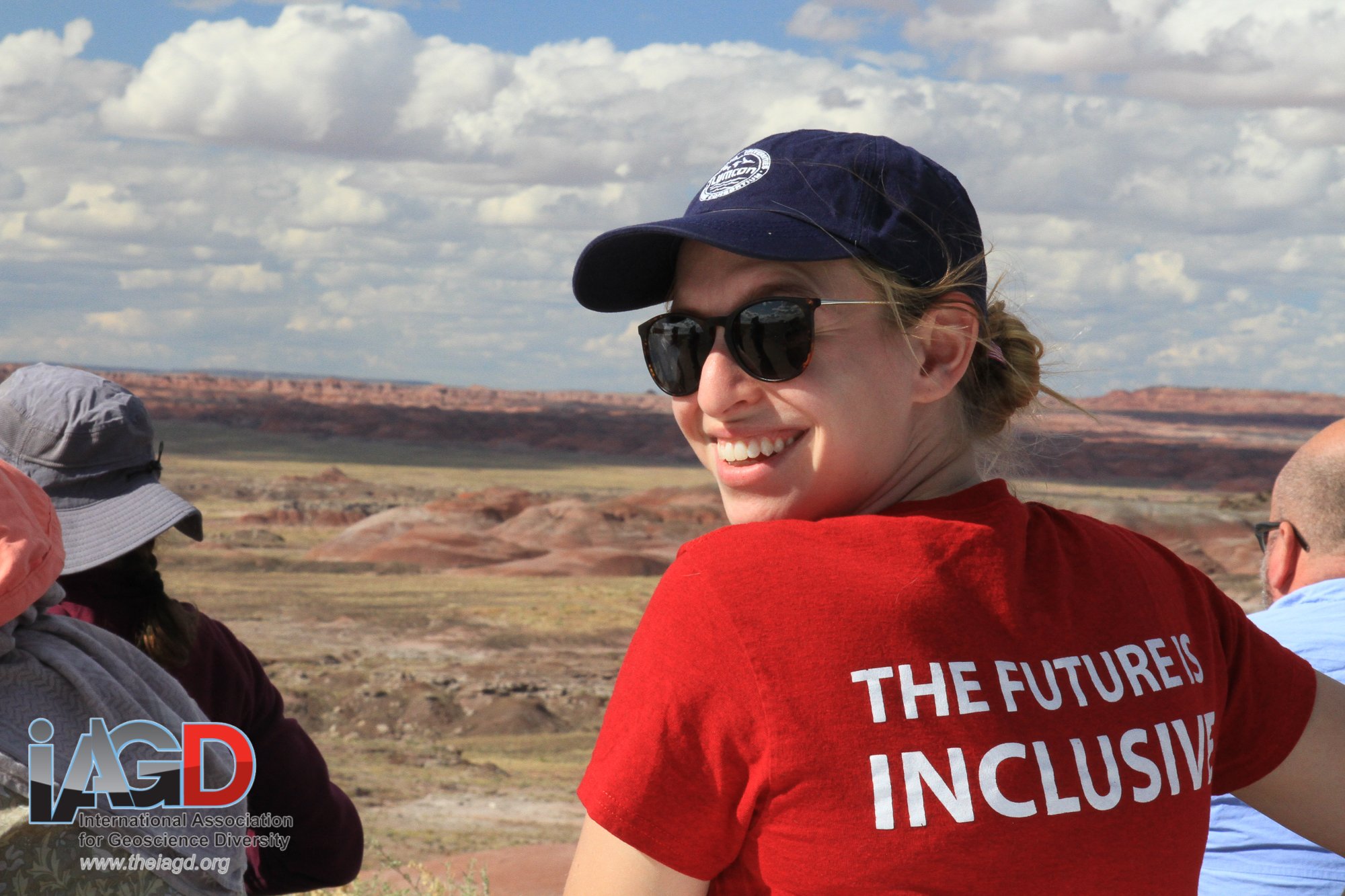 a woman wearing a hat and sunglasses is turning around to the left. her shirt says "the future is inclusive."