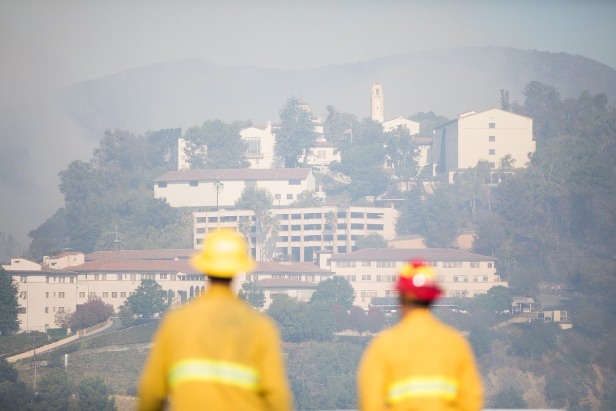 October 28, 2019: Two firefighters look at a large building slightly clouded by smoke.
