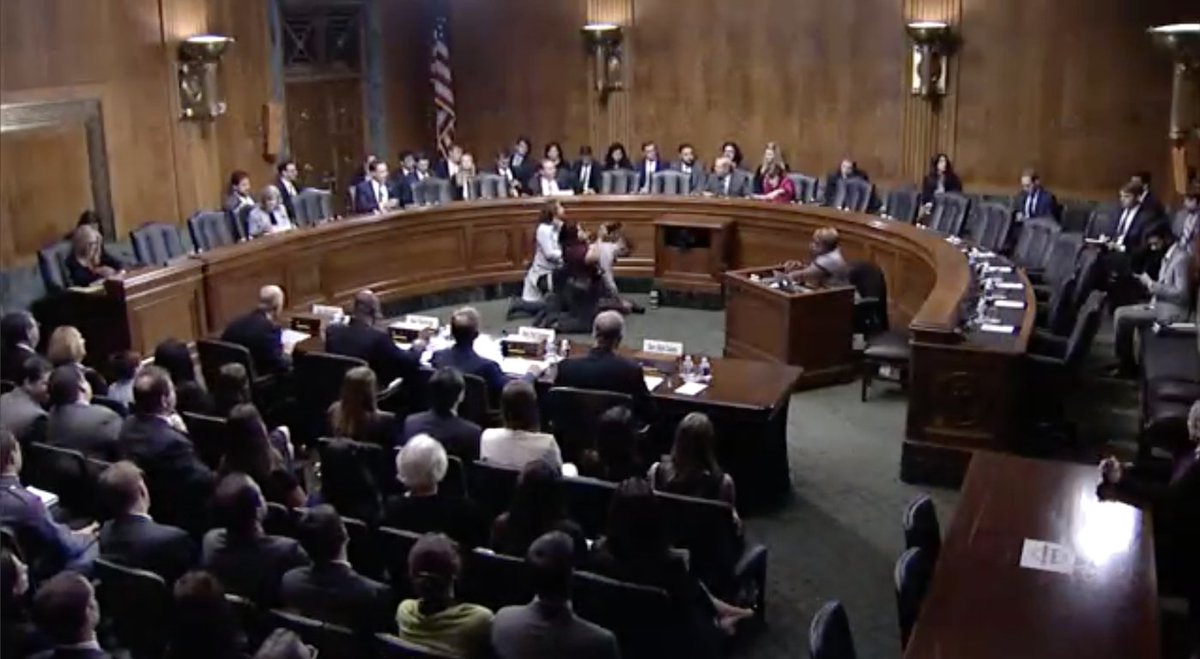 Senate Judiciary Committee hearing room, showing senators sitting on the dais, additional senators sitting behind the desk ready to introduce nominees, and people watching in the audience.
