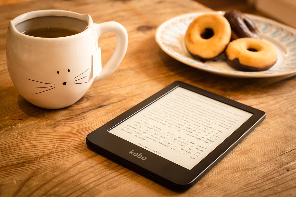 a cup of coffee, plate of donuts and eReader tablet all displayed on a kitchen table next to each other
