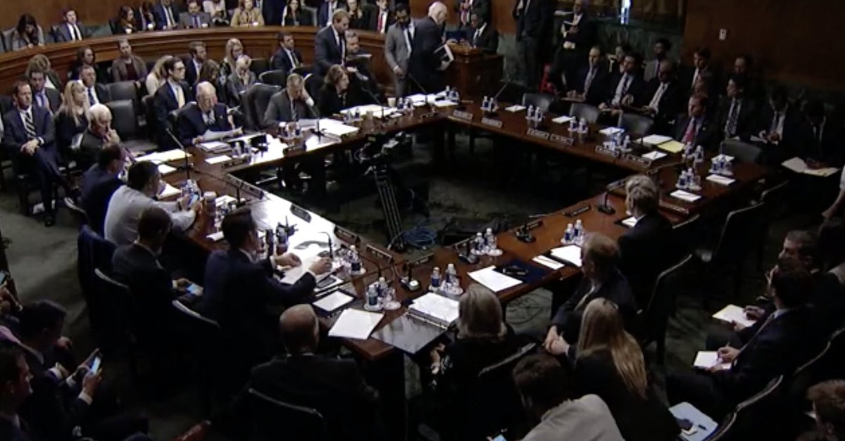 Senate Judiciary Committee hearing room shows senators sitting around a large table with people watching in the audience.