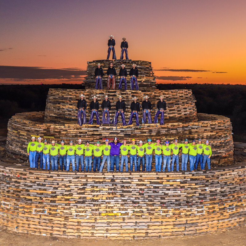 Tarleton Plowboys and recruits on top of the bonfire stack with sun setting behind them.