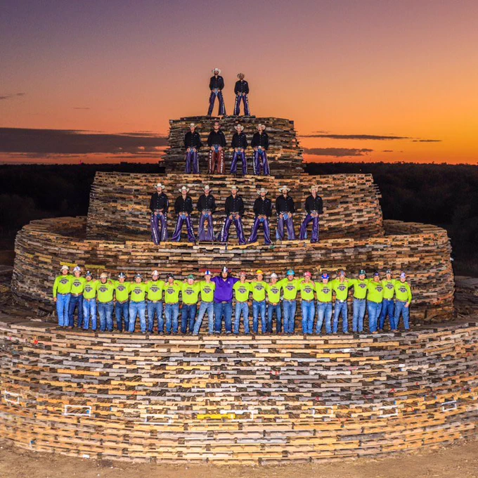 Tarleton Plowboys and recruits on top of the bonfire stack with sun setting behind them.