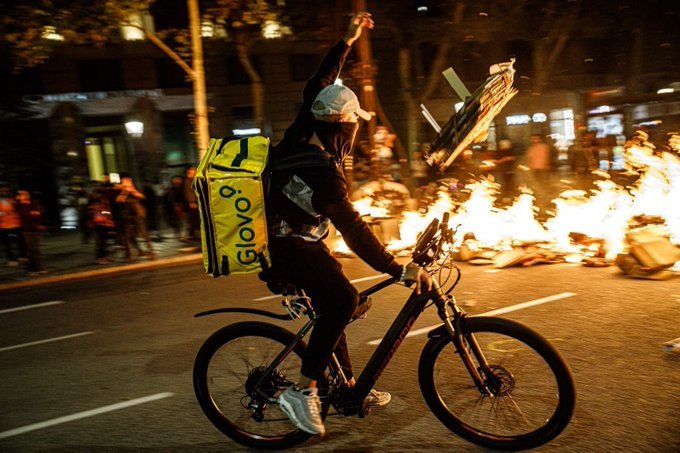 paratcha78's tweet photo. Rider de Glovo alimenta una hoguera durante los disturbios del viernes noche en Barcelona. Foto de @_ittos_ https://t.co/CI0cW2RQ4K