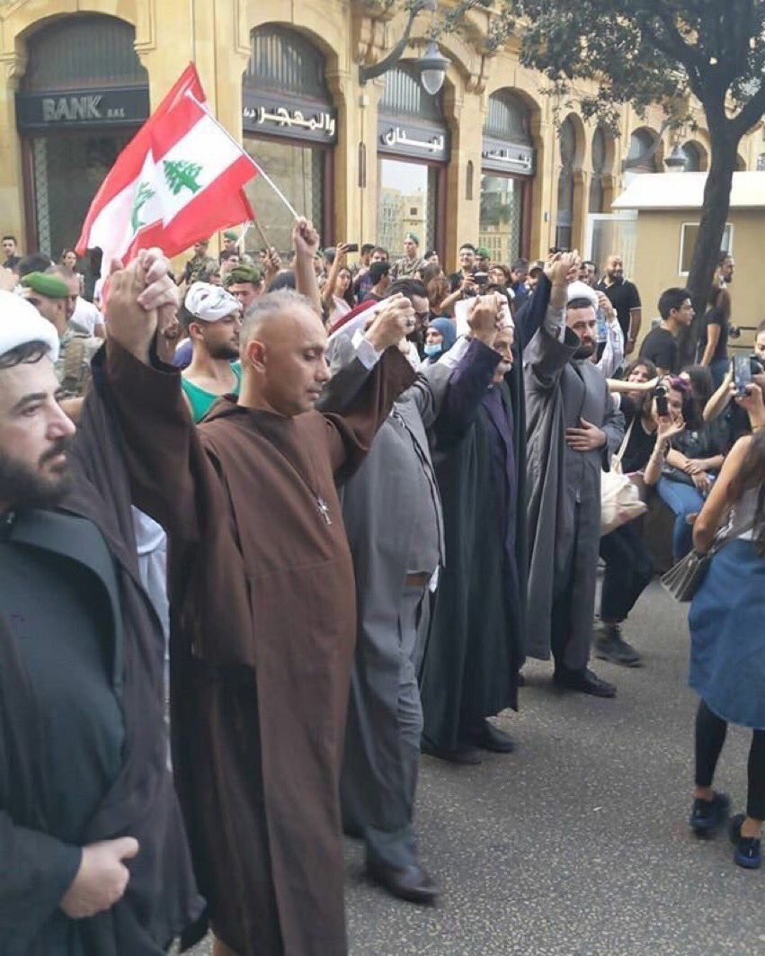 christian, muslim, sunni, and druze religious leaders holding hands and protesting in front of a mosque and church 