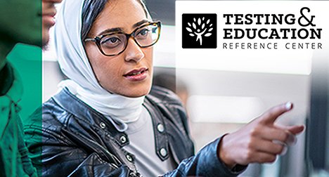a woman wearing a head scarf pointing at a computer screen, demonstrating to smoeone sitting next to her