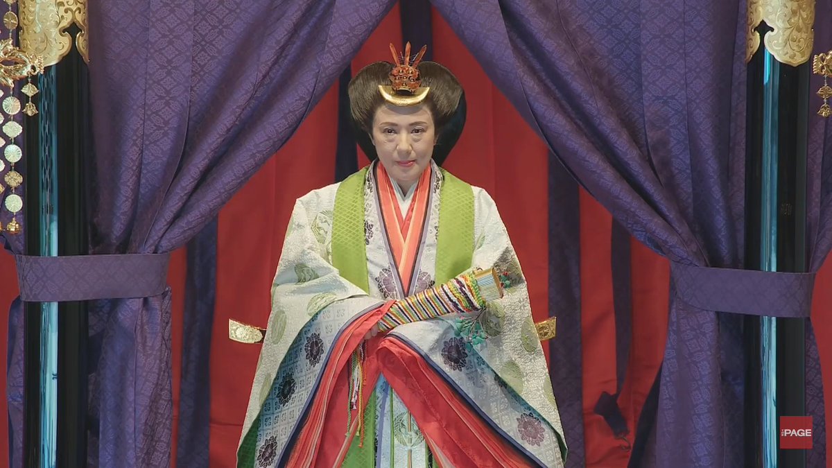 Empress Masako is wearing many-layered jūnihitoe robes and carries a fan. Her hair is in the elaborate osuberakashi style, held with golden kanzashi ornamental pins.