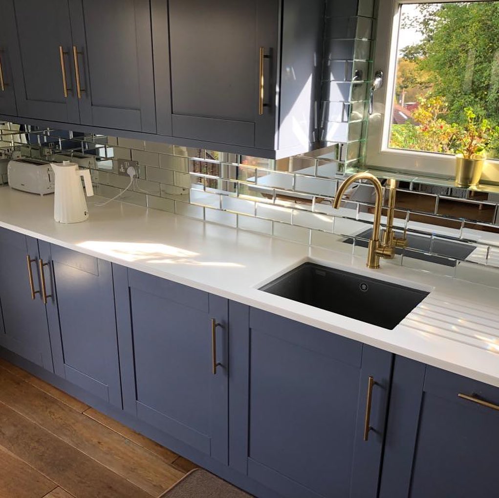 #MISTRALHighlights - The garden-facing window floods the room with natural light that reflects upon mirrored tiles, making this kitchen gleam with class. MISTRAL Glacier work surfaces show their versatility as they marry together beautiful blue cabinetry and golden accents.