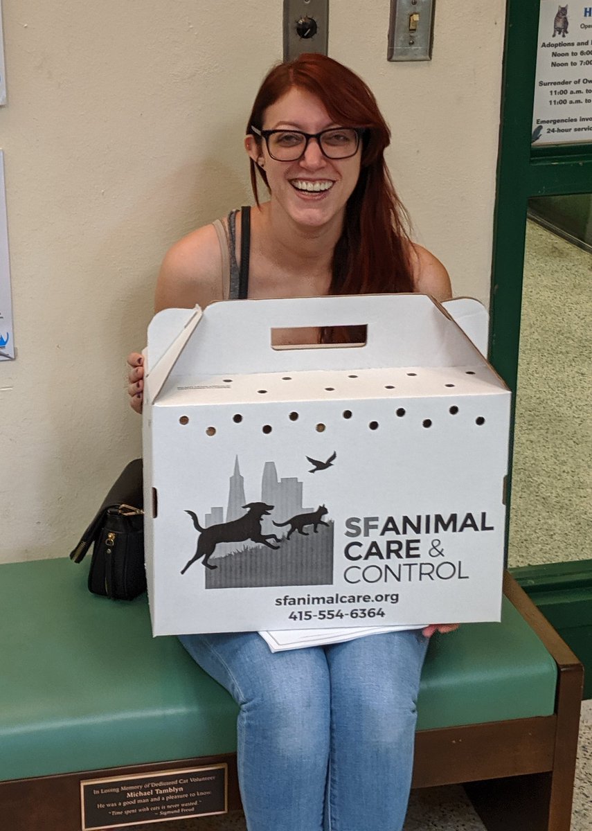 Very a happy woman sitting, holding a cat carrier on her lap.