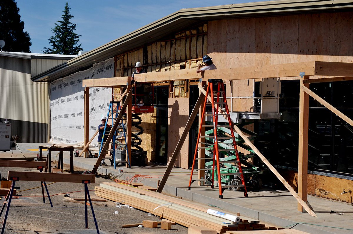 Two construction workers are installing beams outside by a building.