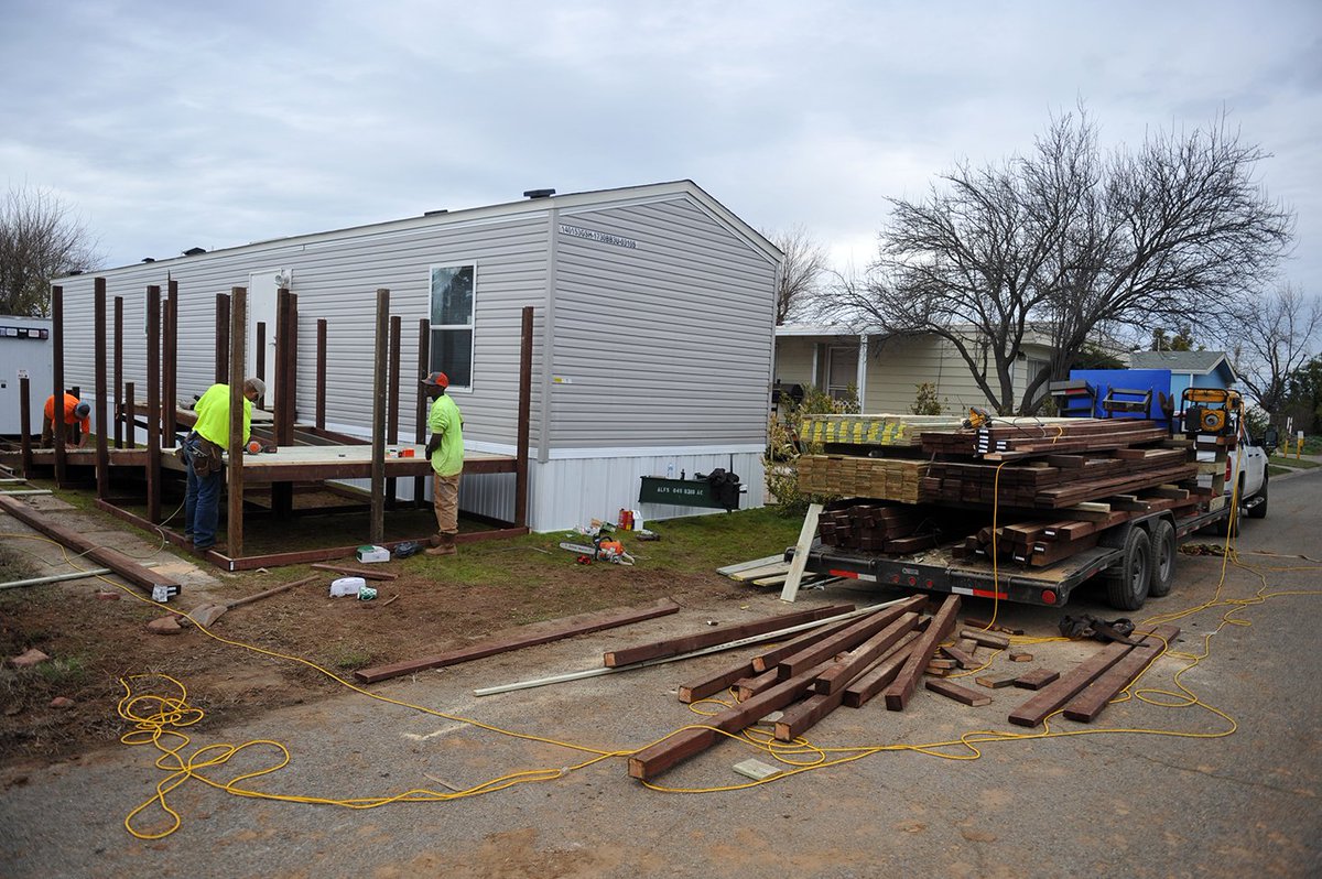Three workers stand outside constructing a ramp behind a home.
