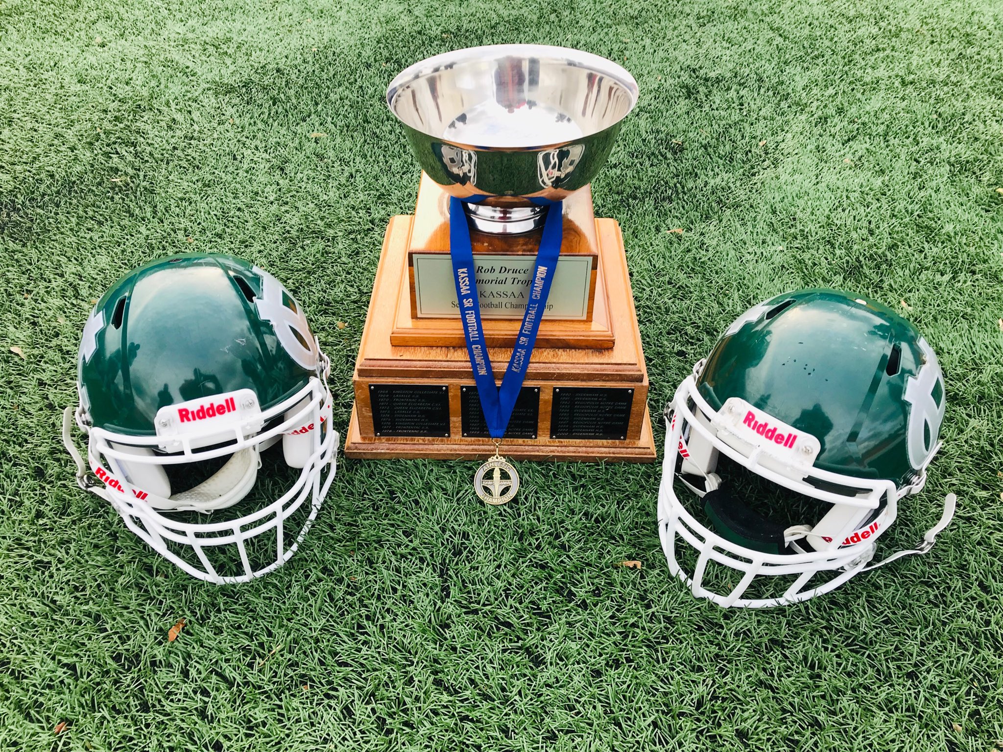 Two Football helmets and a trophy with medal attached.