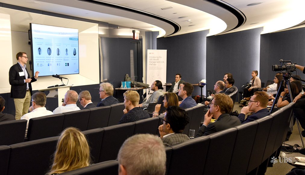 A man stands at a podium, pitching his fintech idea to an auditorium full of attendees at UBS. 