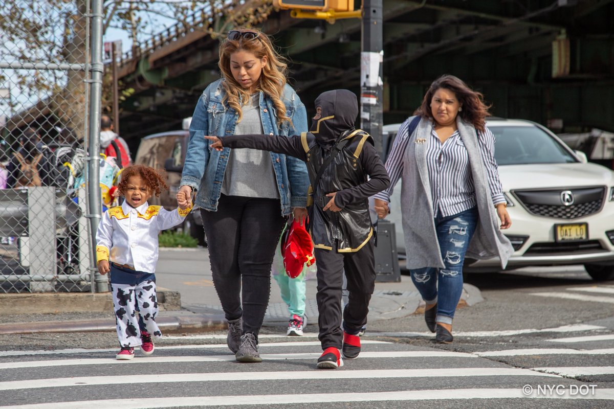 Parents and kids in costumes walk across the street in a crosswalk on a fall day
