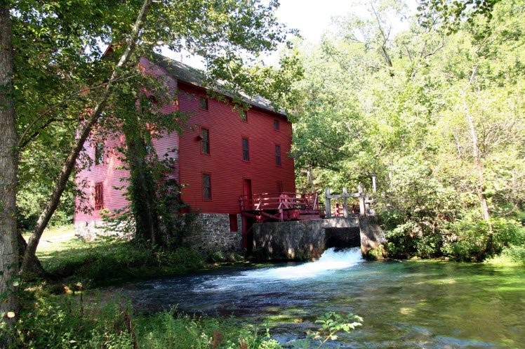 Alley Mill in Ozark National Scenic Riverways is an historic, 3-story, red structure on a stone foundation next to a flowing creek and stone millworks. NPS file photo.