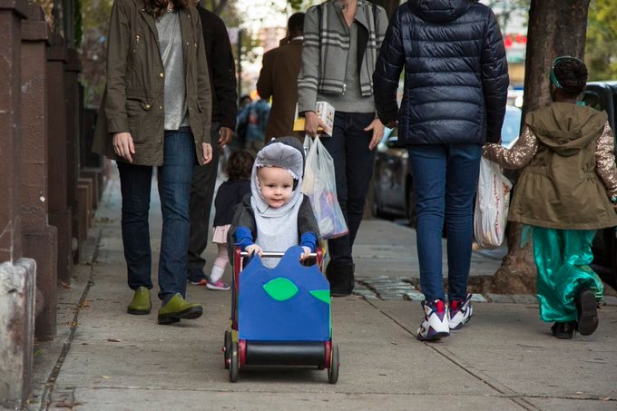 several people including a baby dressed as a shark walk down the street.