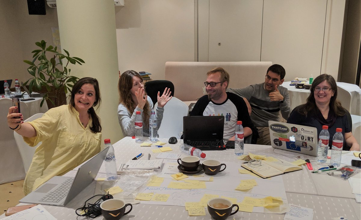 Three women and two men gathered around a table of sticky notes, computers, and coffee cups.