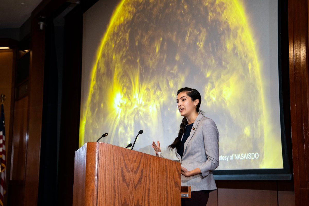 woman at a podium in front of a picture of the sun