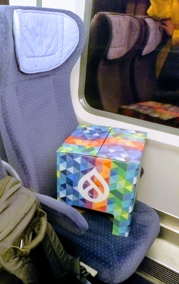 DrupalCon-branded cardboard stool on a train seat.